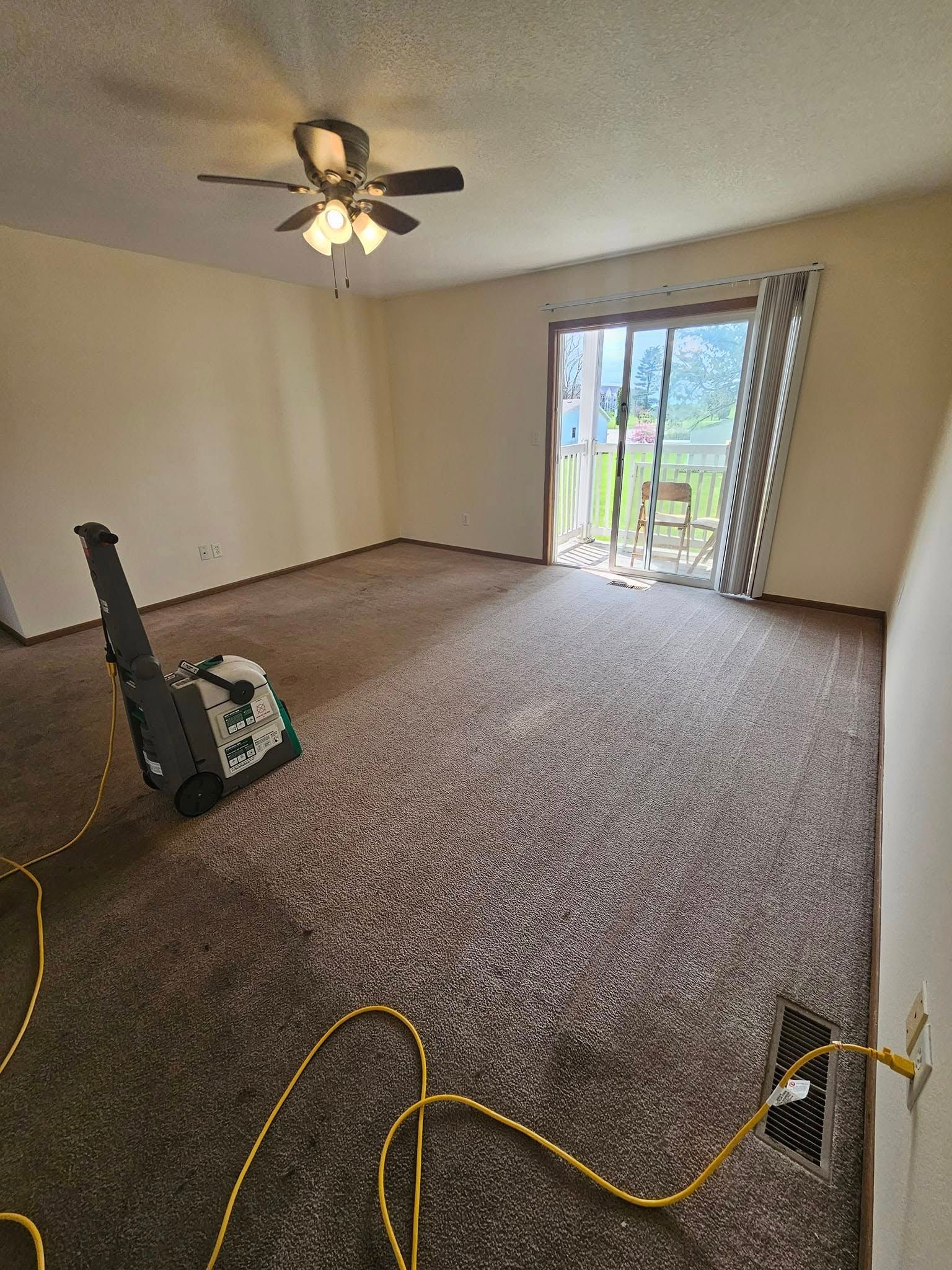 An empty living room with a ceiling fan and a sliding glass door.
