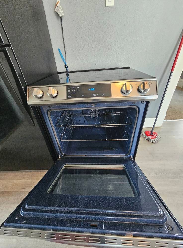 A stove with the door open and a mop in the background.