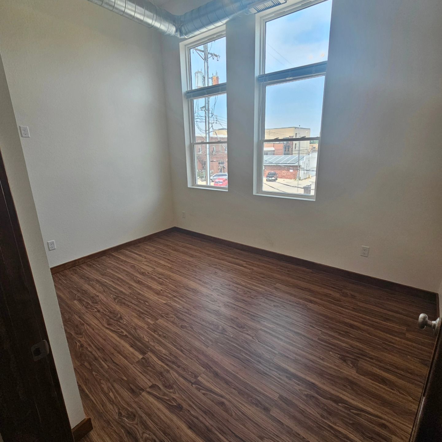 An empty room with hardwood floors and two windows.