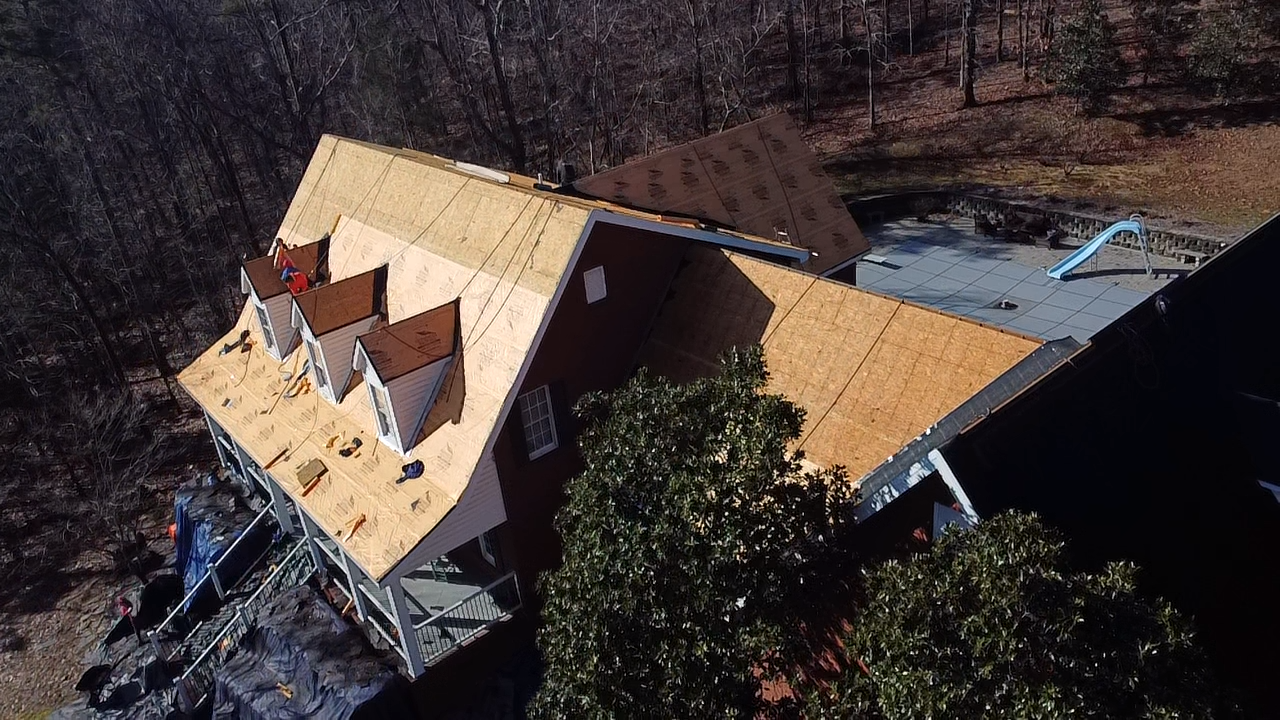 Aerial view of a house undergoing roof renovations, showing bare plywood sheathing and several dormers under construction.