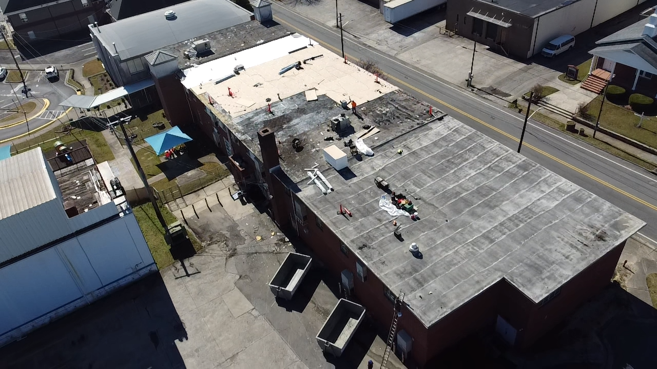 An aerial view of a rectangular building with a partially replaced tan roof next to a grey, weathered section.