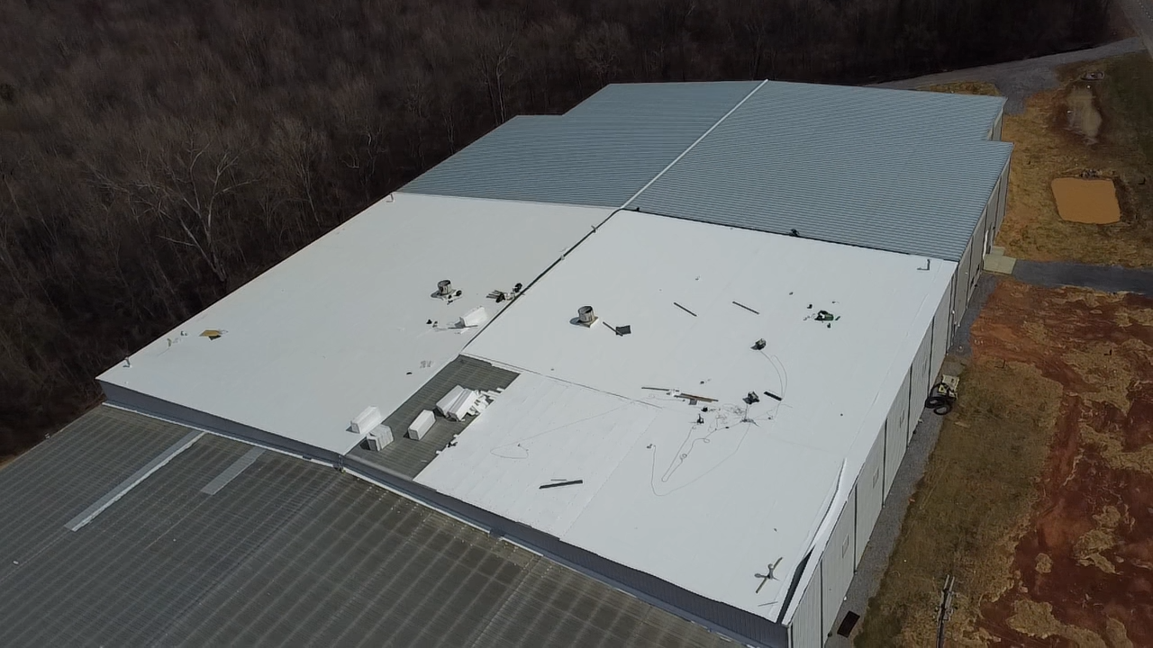 Aerial view of a rectangular warehouse roof showing scattered debris and damaged sections.