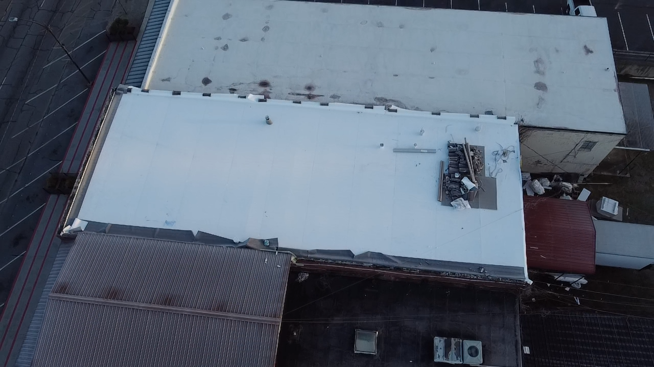 An aerial view of a large building roof, showing a bright white section, a darker tiled area, and mechanical equipment.