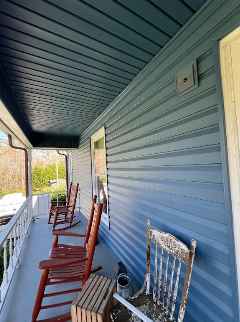 A blue-sided porch featuring several wooden rocking chairs and a small weathered wooden chair.