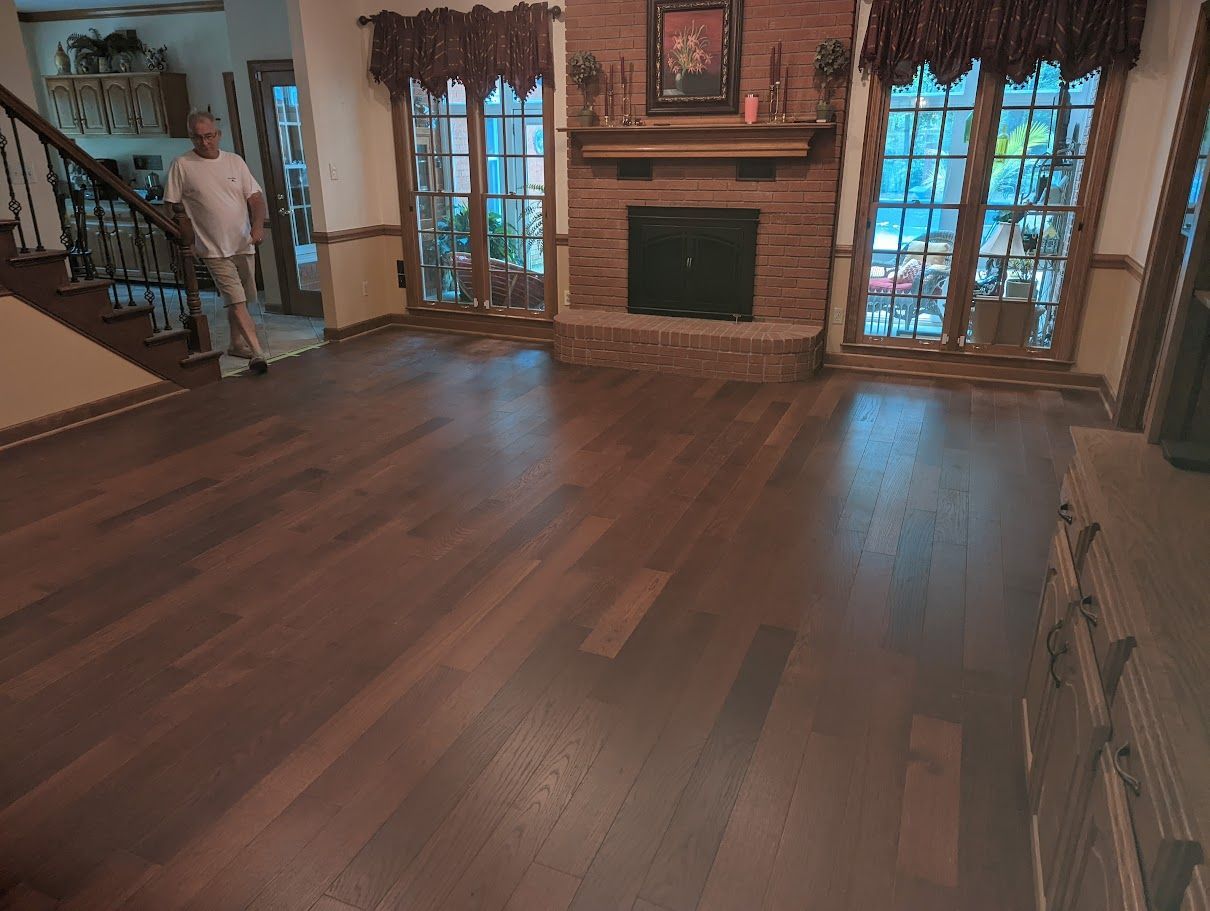 A man is standing in a living room with hardwood floors and a fireplace.