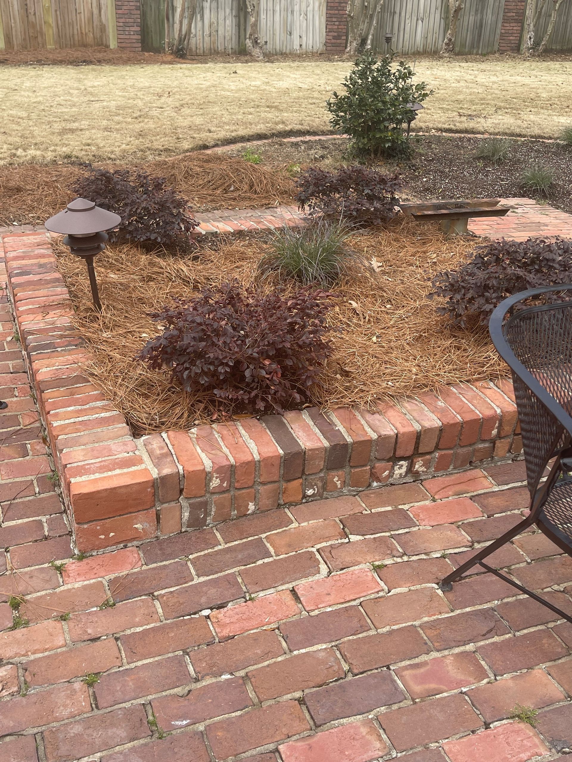 A brick patio with a table and chairs and a garden in the background.