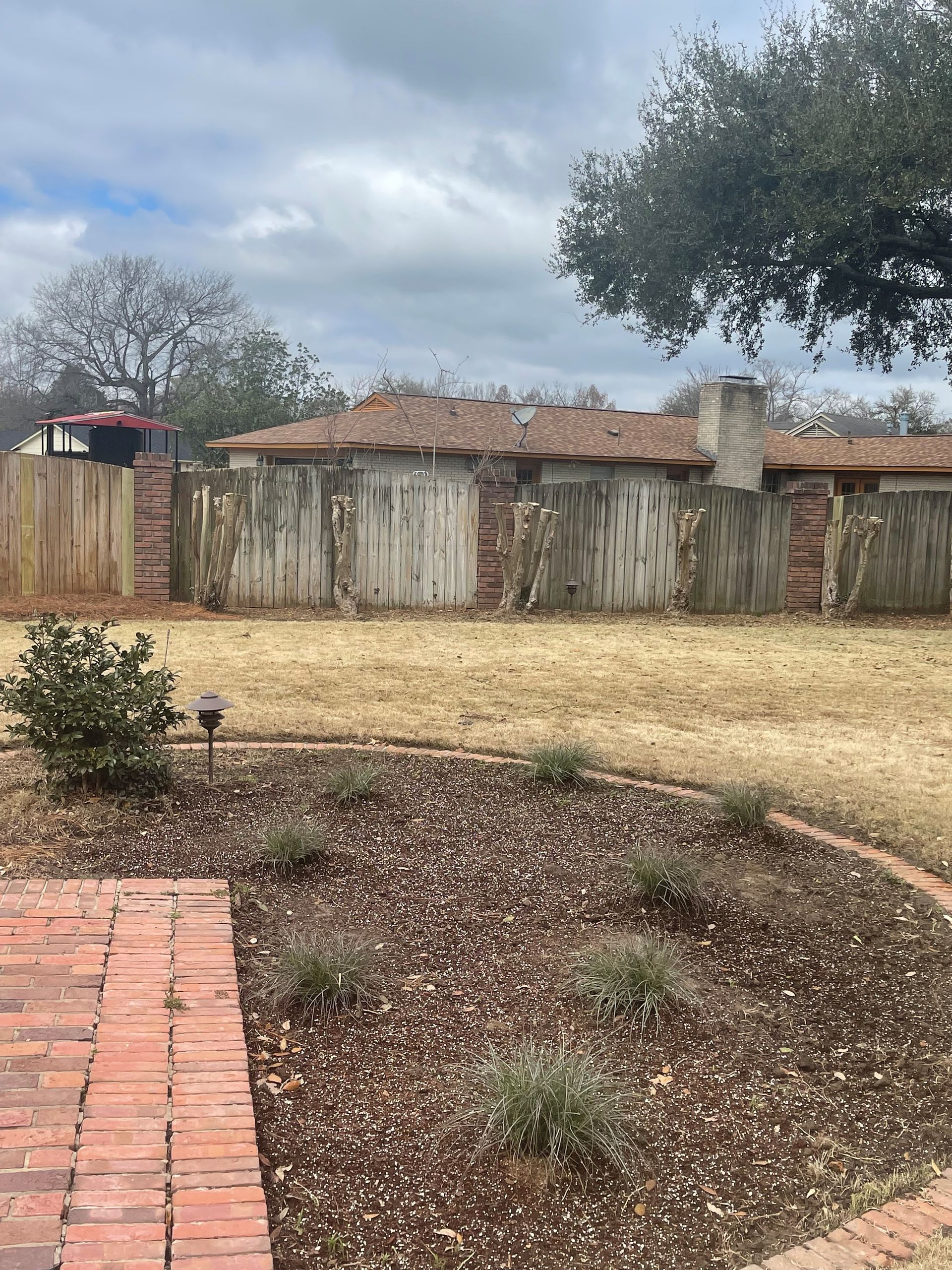 A brick walkway leading to a house with a fence in the background.
