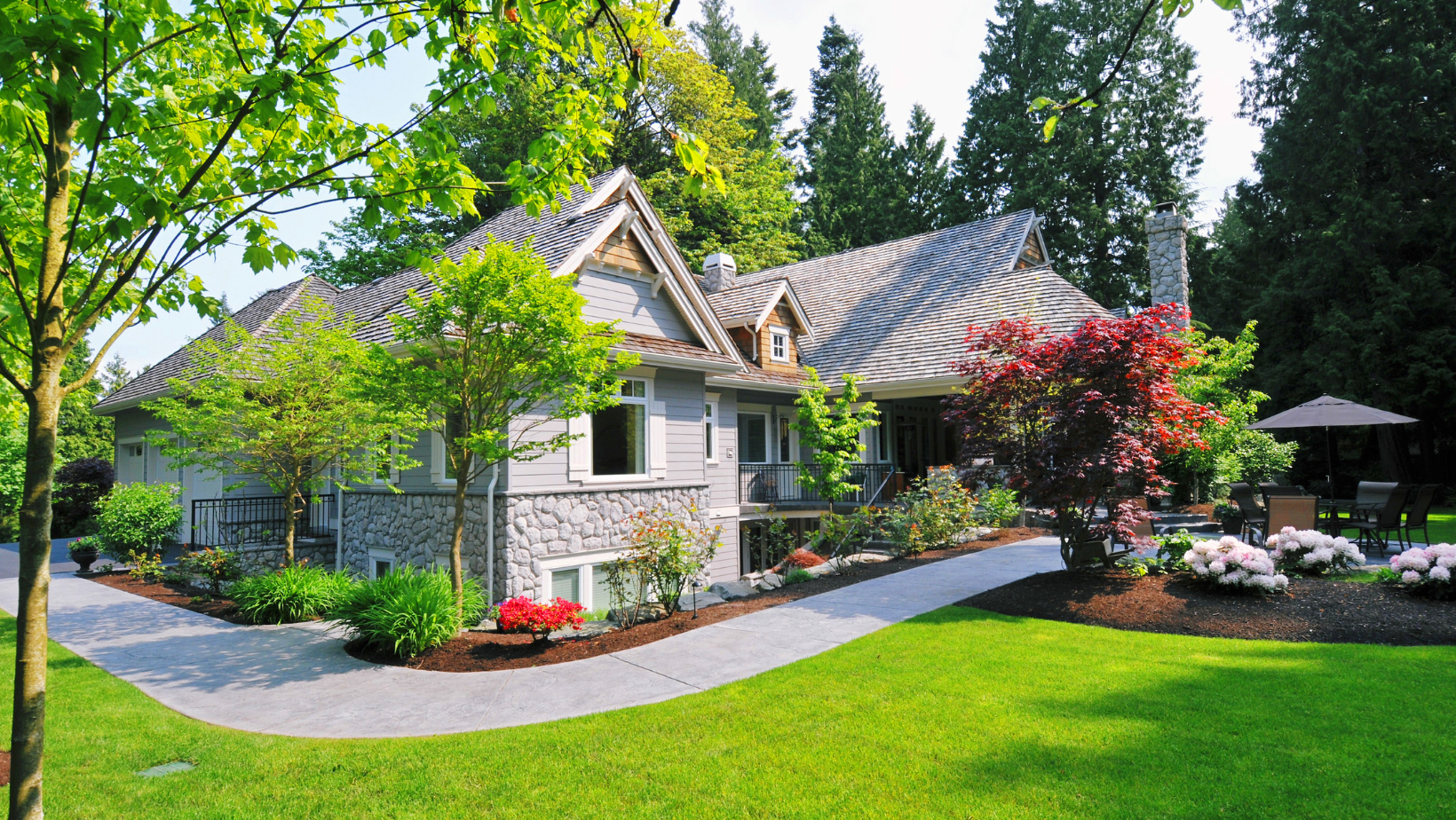 Stone cottage with curved roof, landscaped garden, and green lawn in bright sunlight