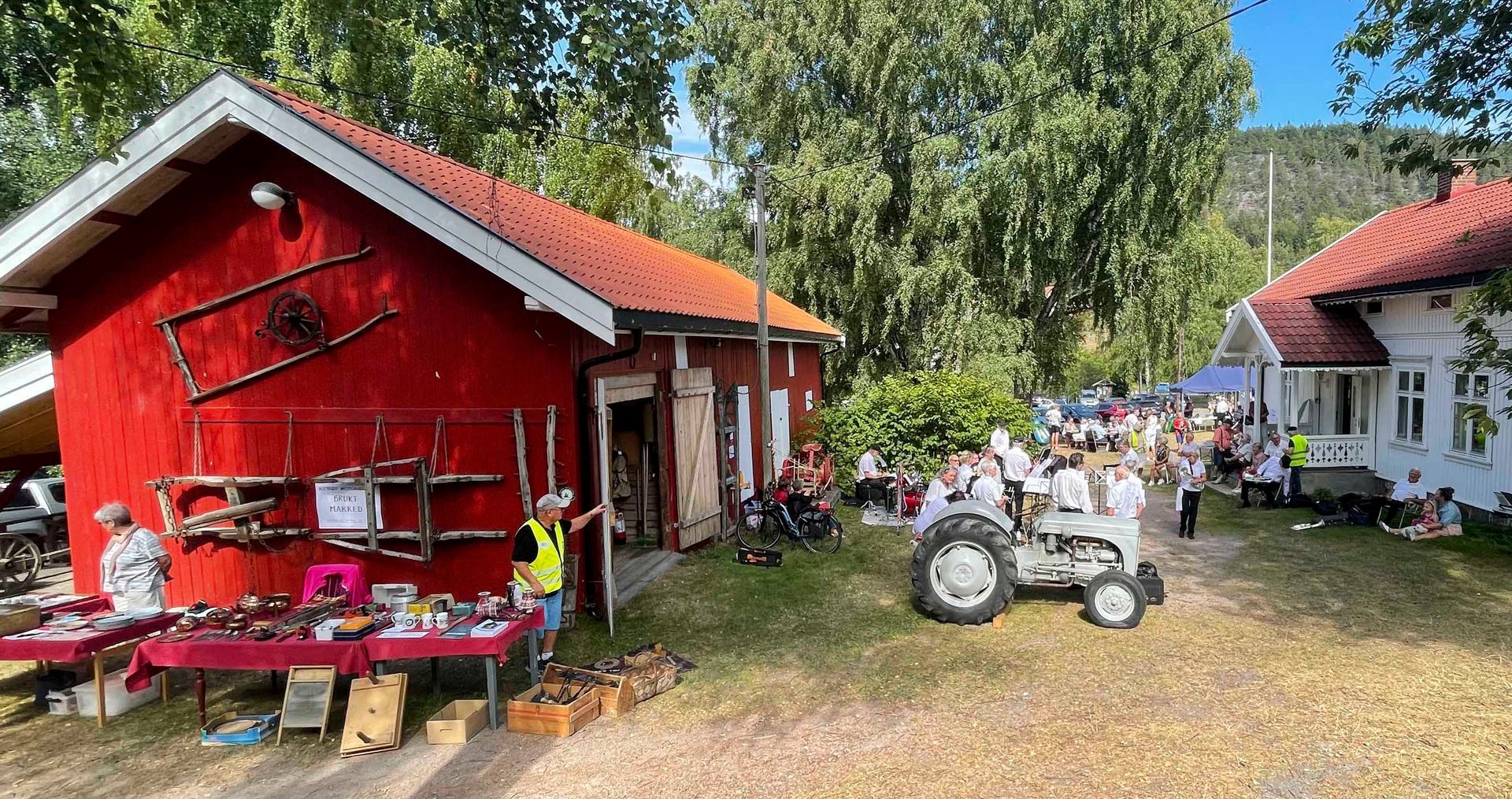 Utendørs loppemarked med røde bygninger, en hvit traktor og mange mennesker som titter.