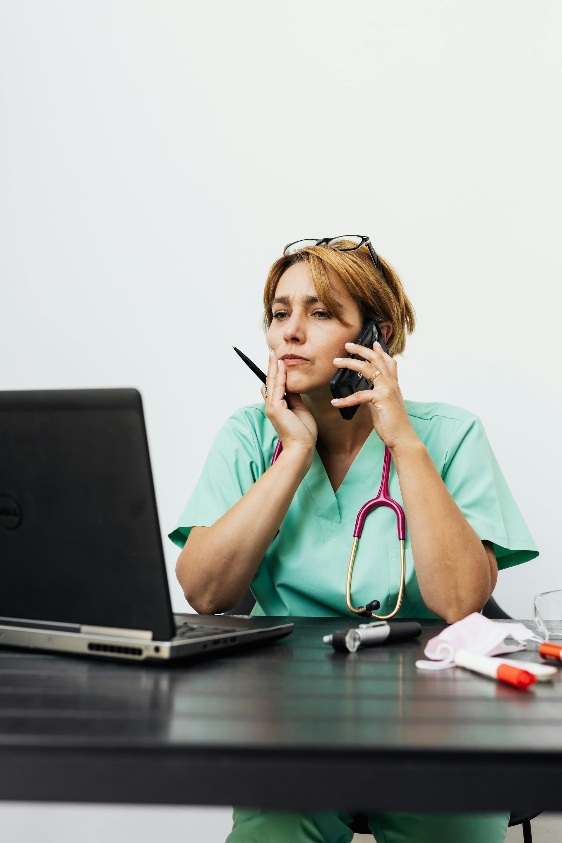 A nurse is talking on a phone while looking at her laptop