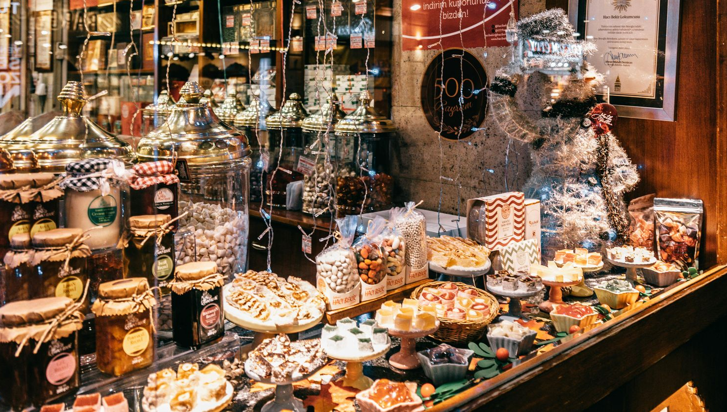 Display of sweets and preserves in a shop window, including jars, cakes, and candies.
