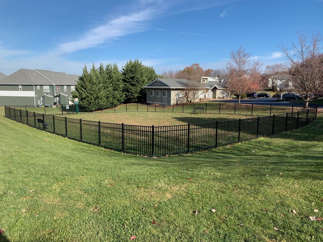 A black fence surrounds a grassy field in front of a house.