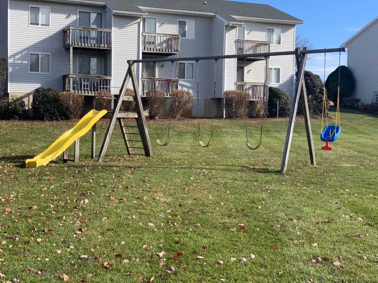 A playground with a slide and swings in front of a house.