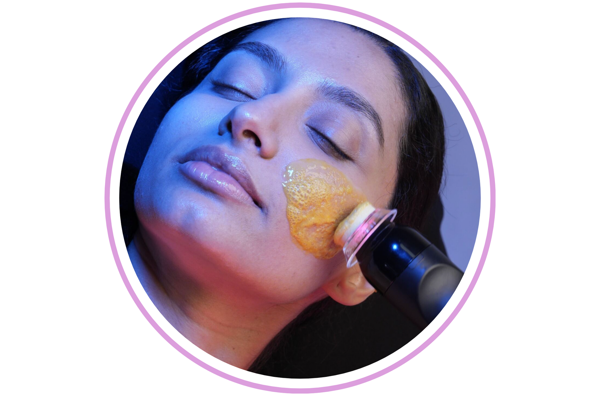 Woman receiving facial treatment with device applying product; indoors, close-up, lit in blue/pink hues.
