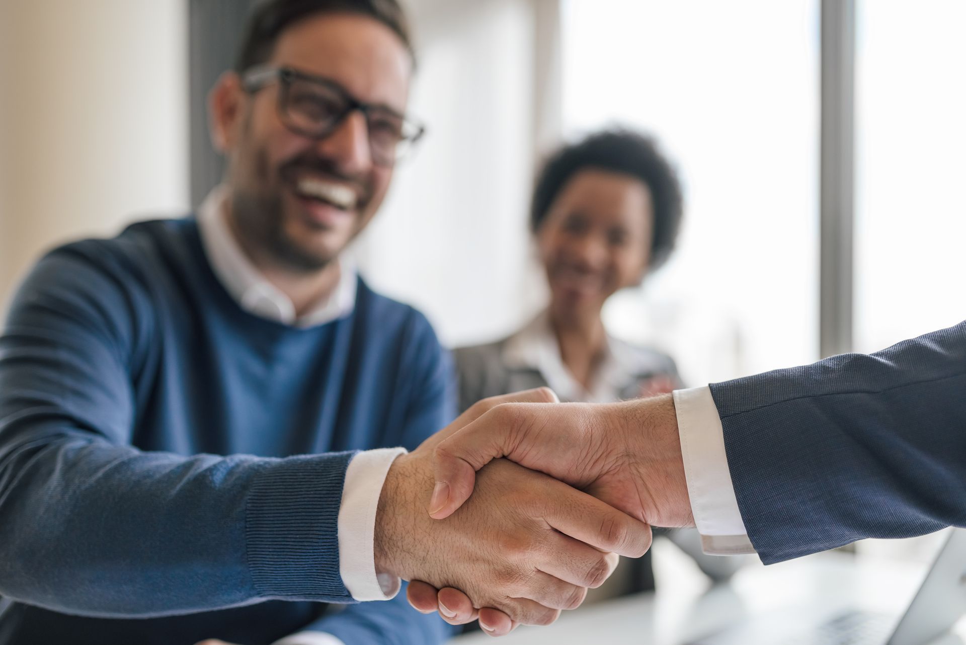 a man in a blue sweater shakes hands with another man in a suit