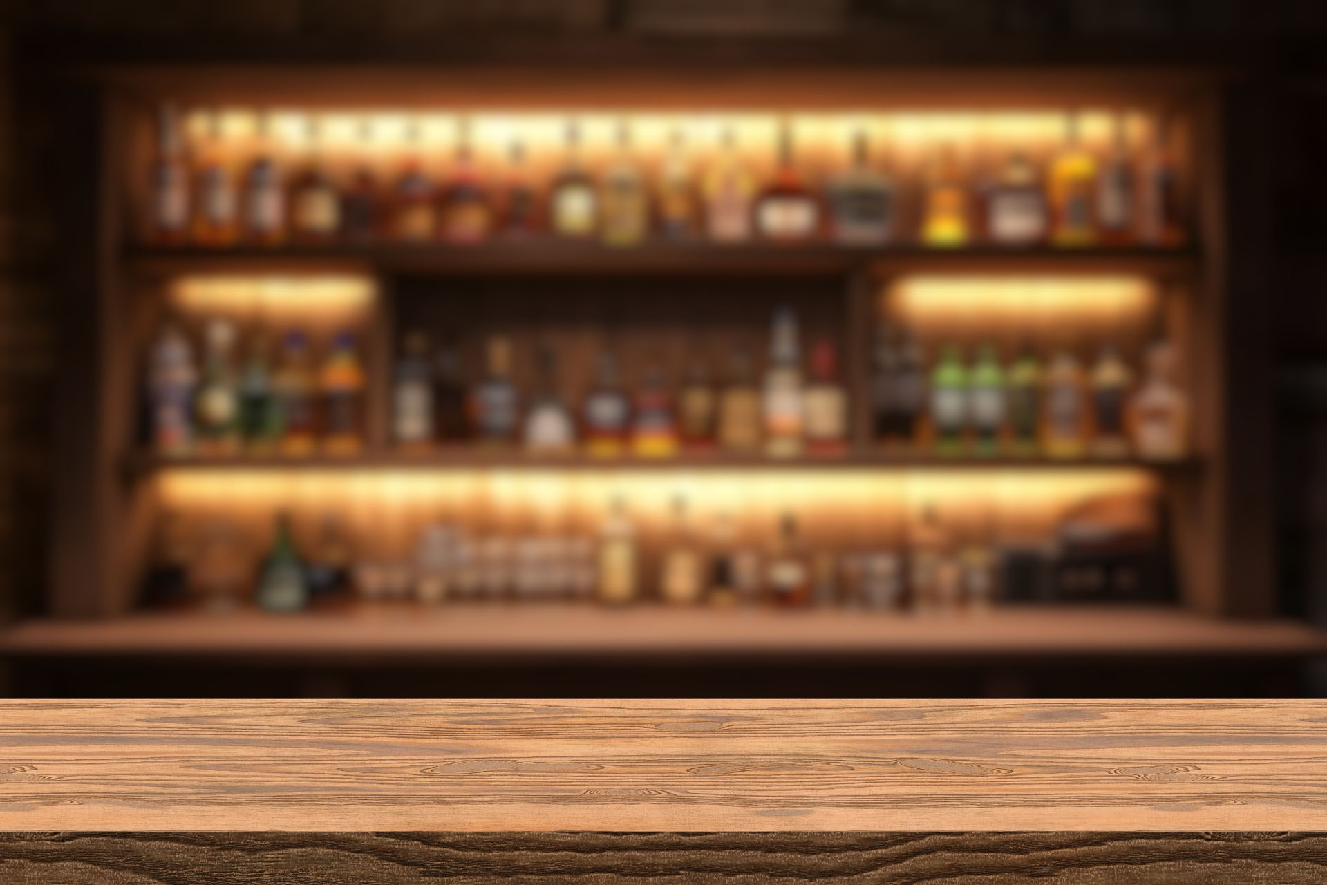 Warmly lit bar shelves with bottles behind a wooden counter