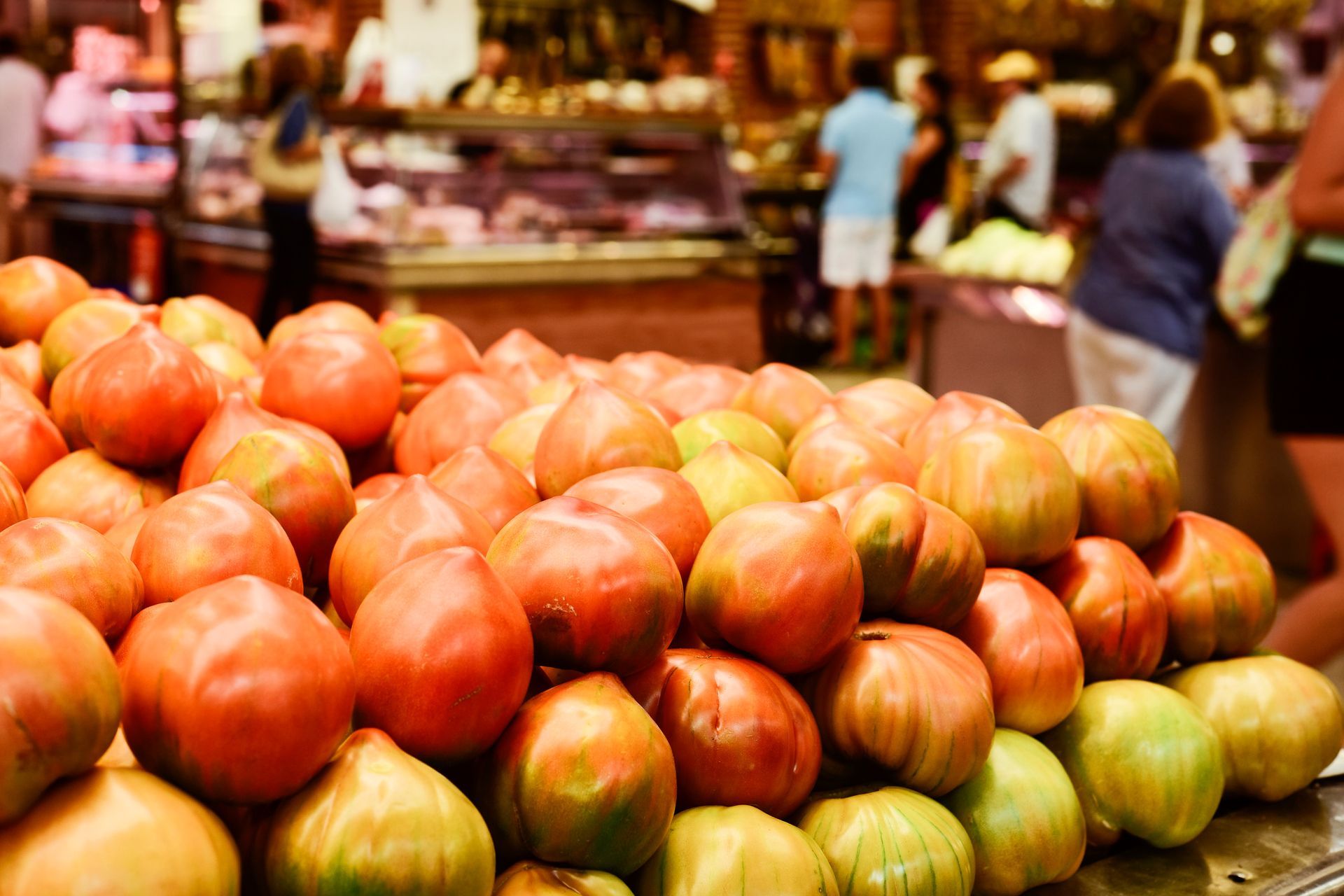 Piles of red and green apples stacked at a busy market stall with blurred shoppers in the background