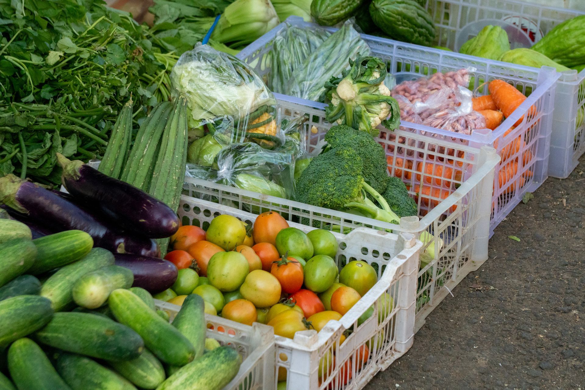 Crates of assorted fresh vegetables and produce stacked outdoors at a market stall
