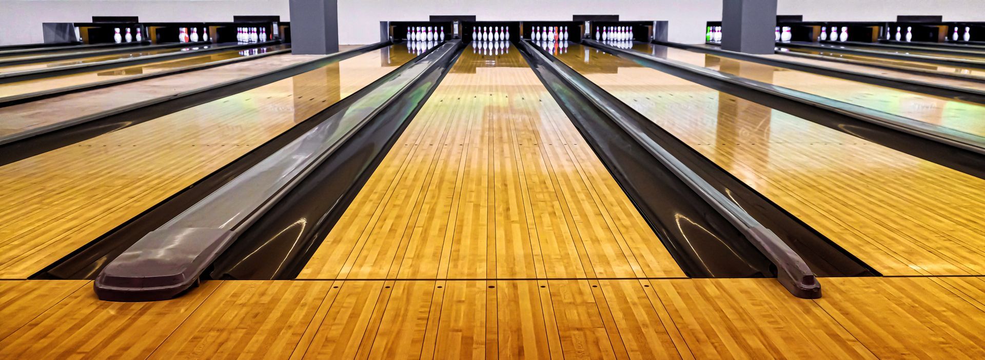 Bowling alley with two lanes, wooden floors, and black gutters leading to distant pins