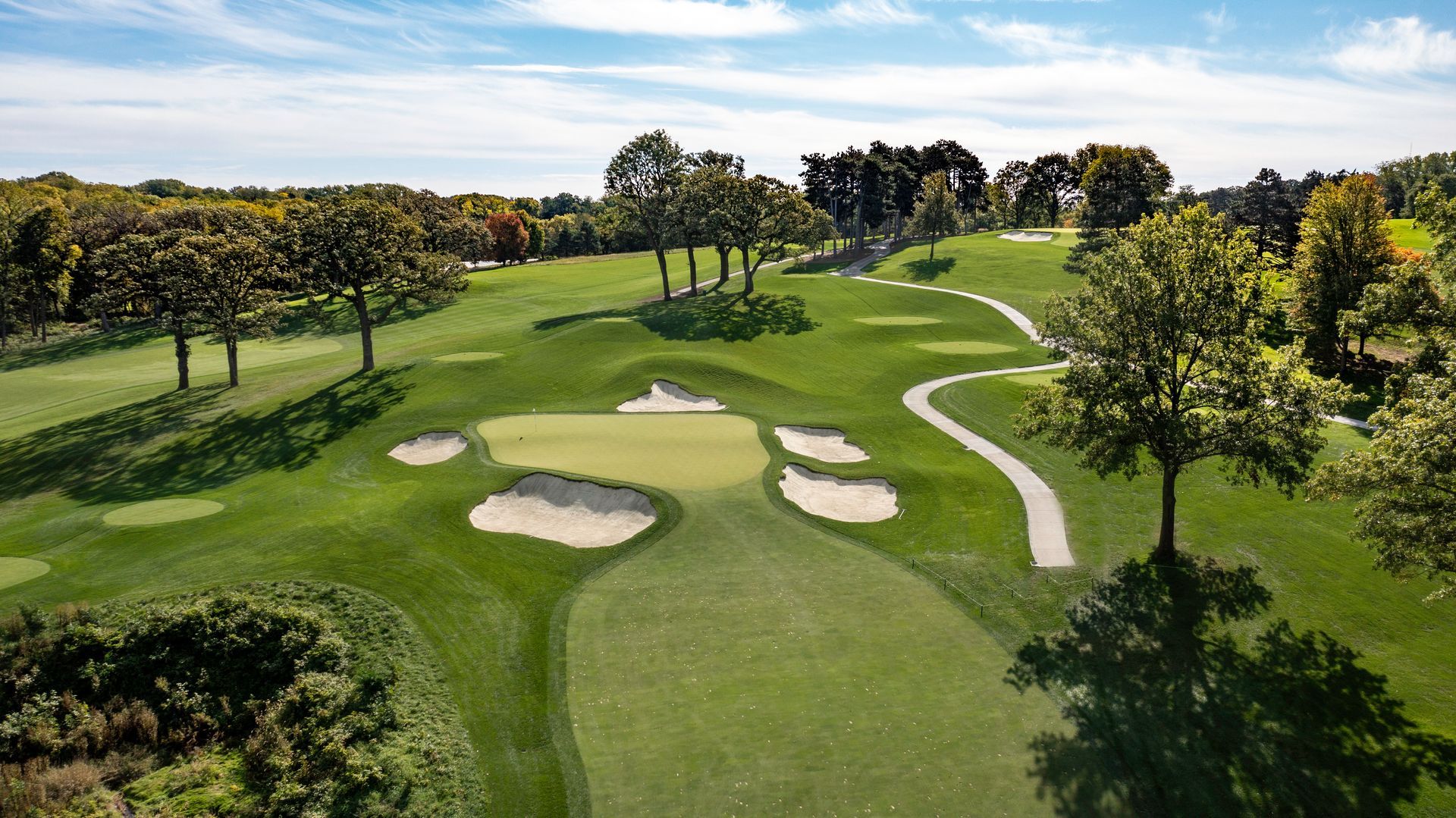Aerial view of a lush golf course with fairway, sand bunkers, and trees under a clear sky