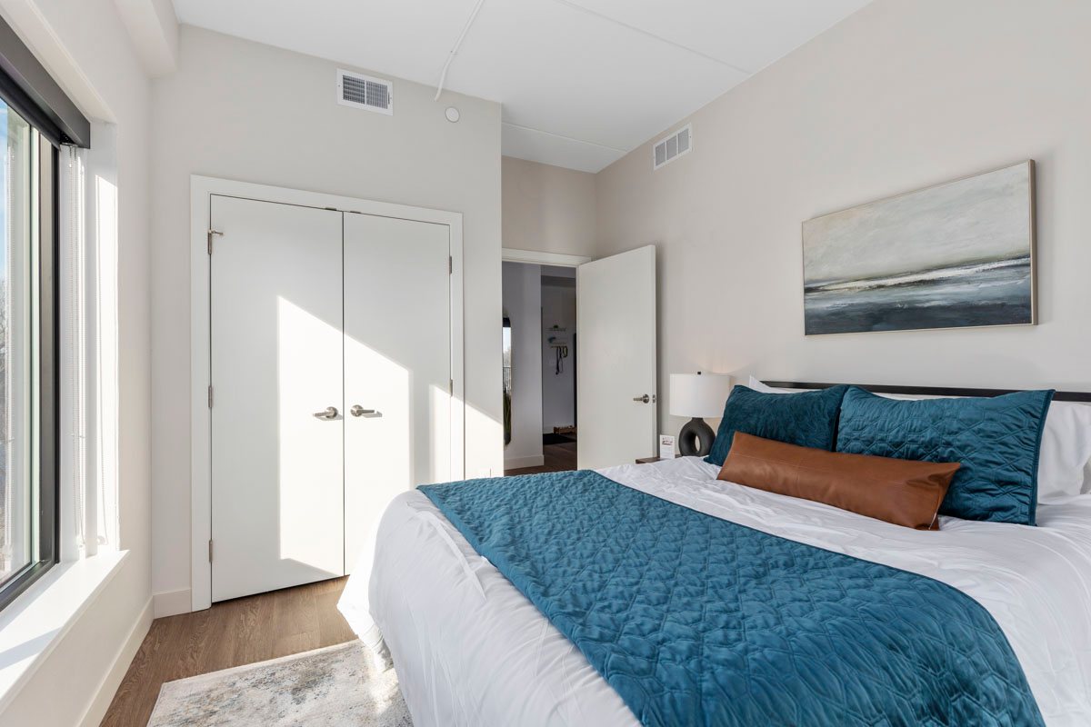 Bright bedroom with a blue bedspread, white closet doors, and large window light.