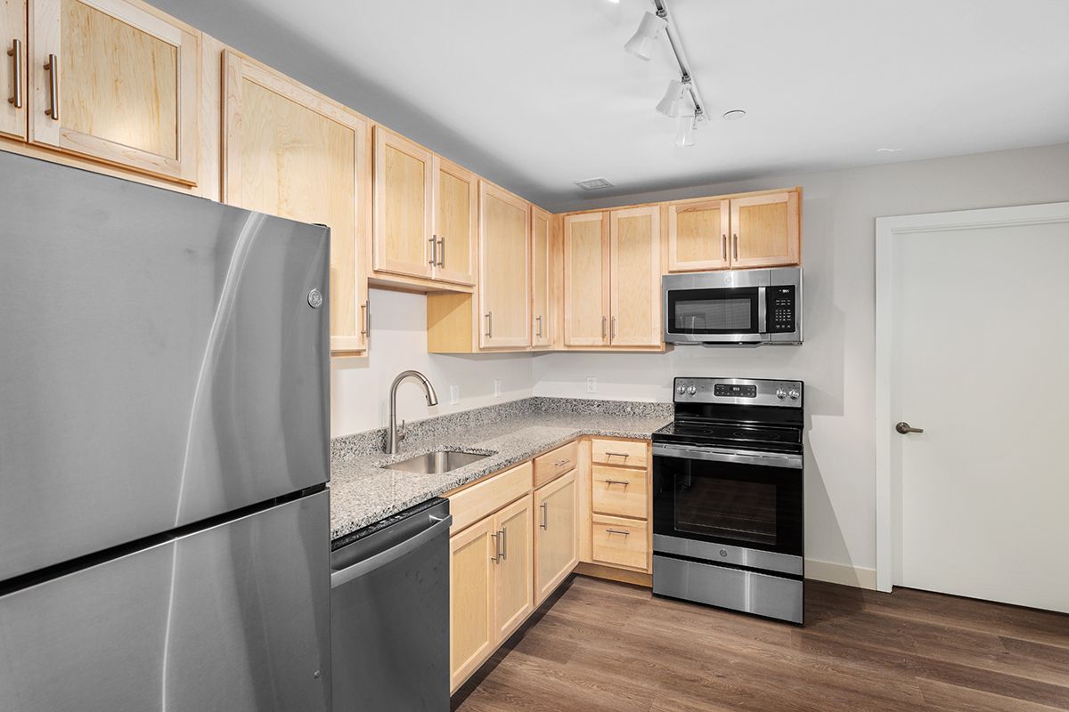 Modern kitchen with stainless steel appliances, light wood cabinets, and granite countertops