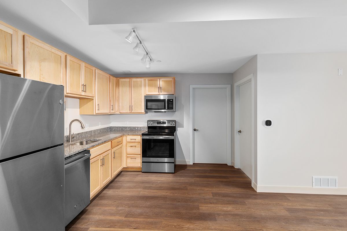Modern kitchen with stainless steel appliances, light wood cabinets, and brown flooring.
