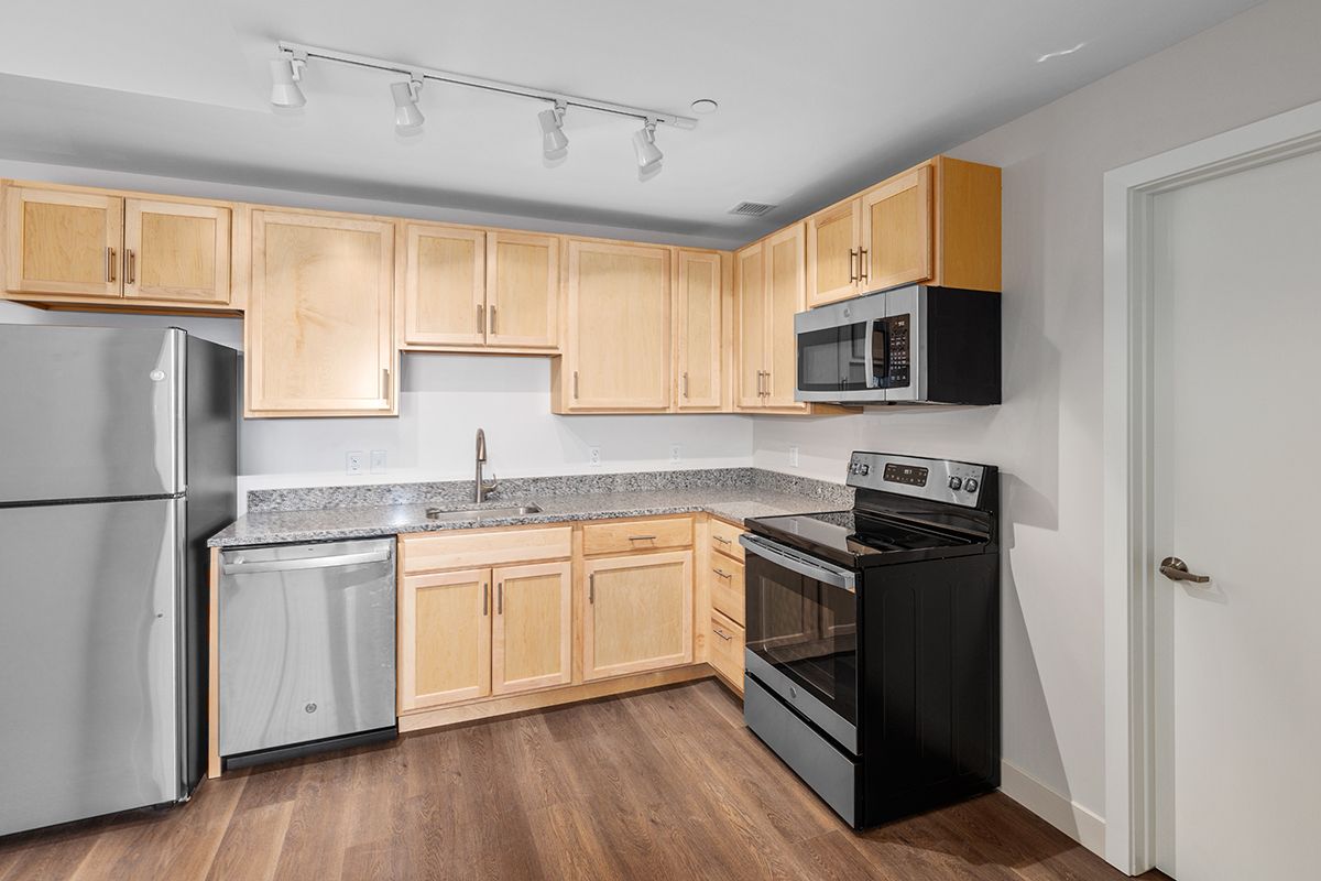 Modern kitchen with light wood cabinets, stainless appliances, black stove, and gray countertops