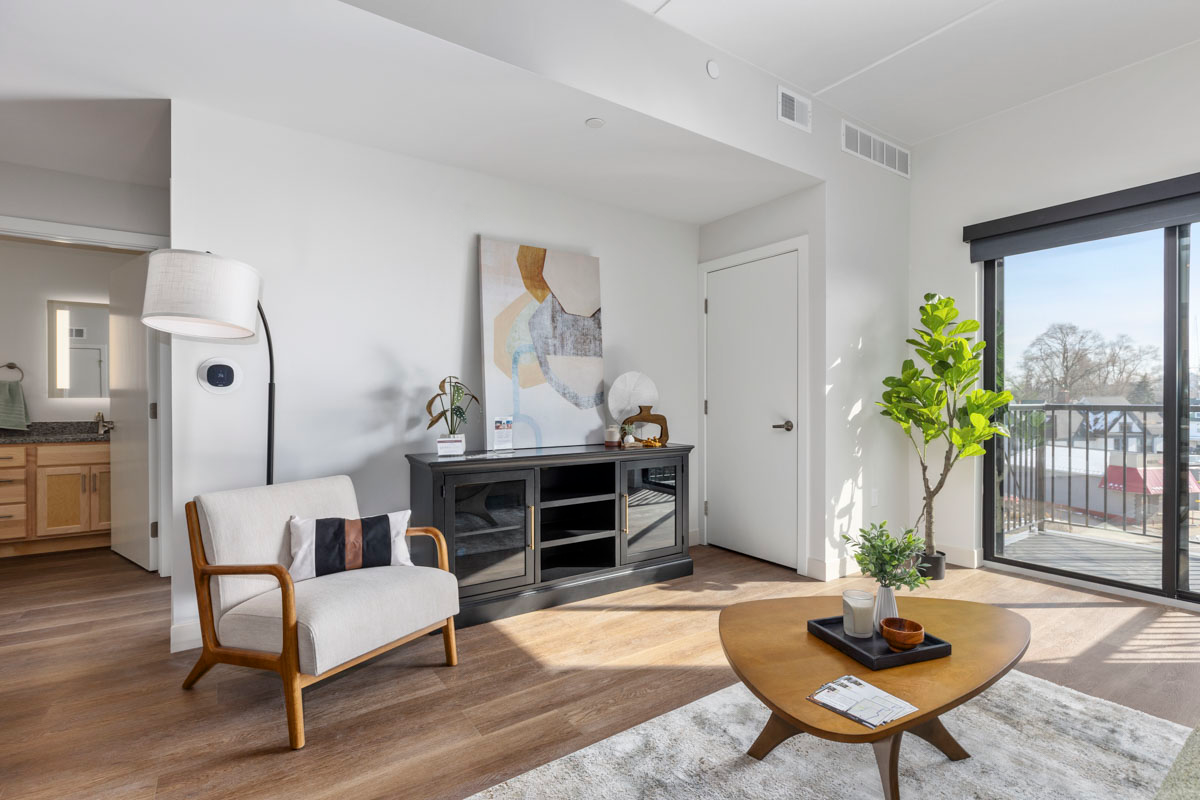 Bright modern living room with white walls, wood floor, sofa, TV console, coffee table, and balcony view.