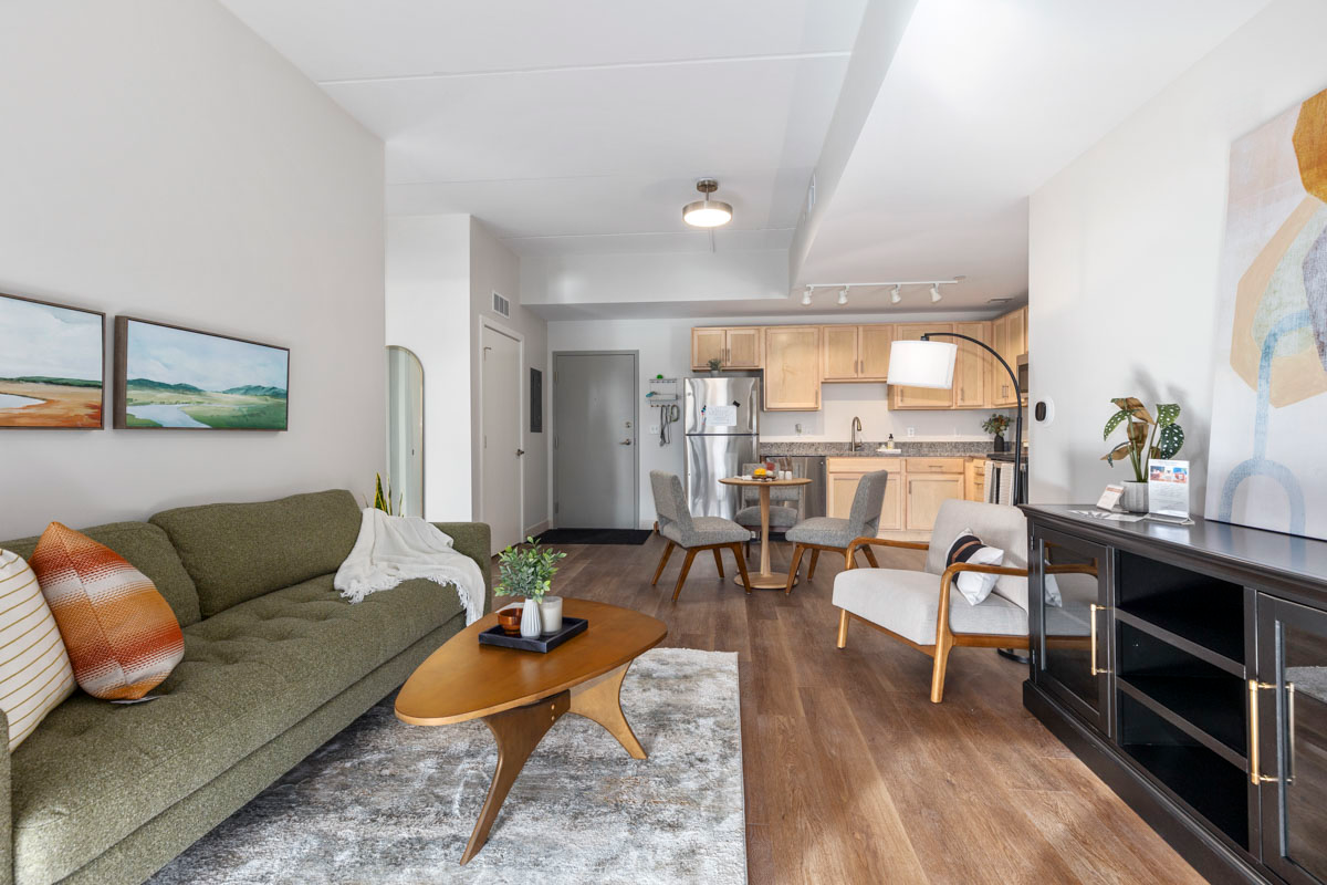 Bright living room with green sofa, coffee table, TV, and open kitchen in the background