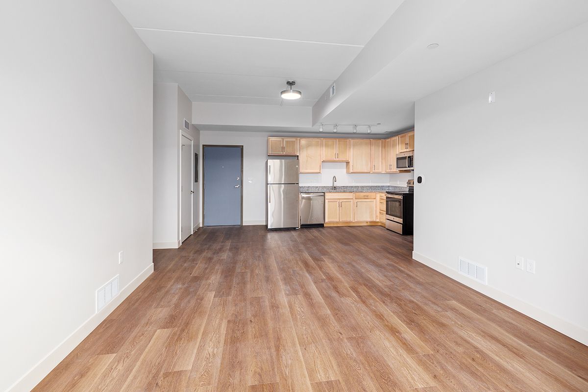 Empty apartment living area with wood floors and a small kitchen in the back