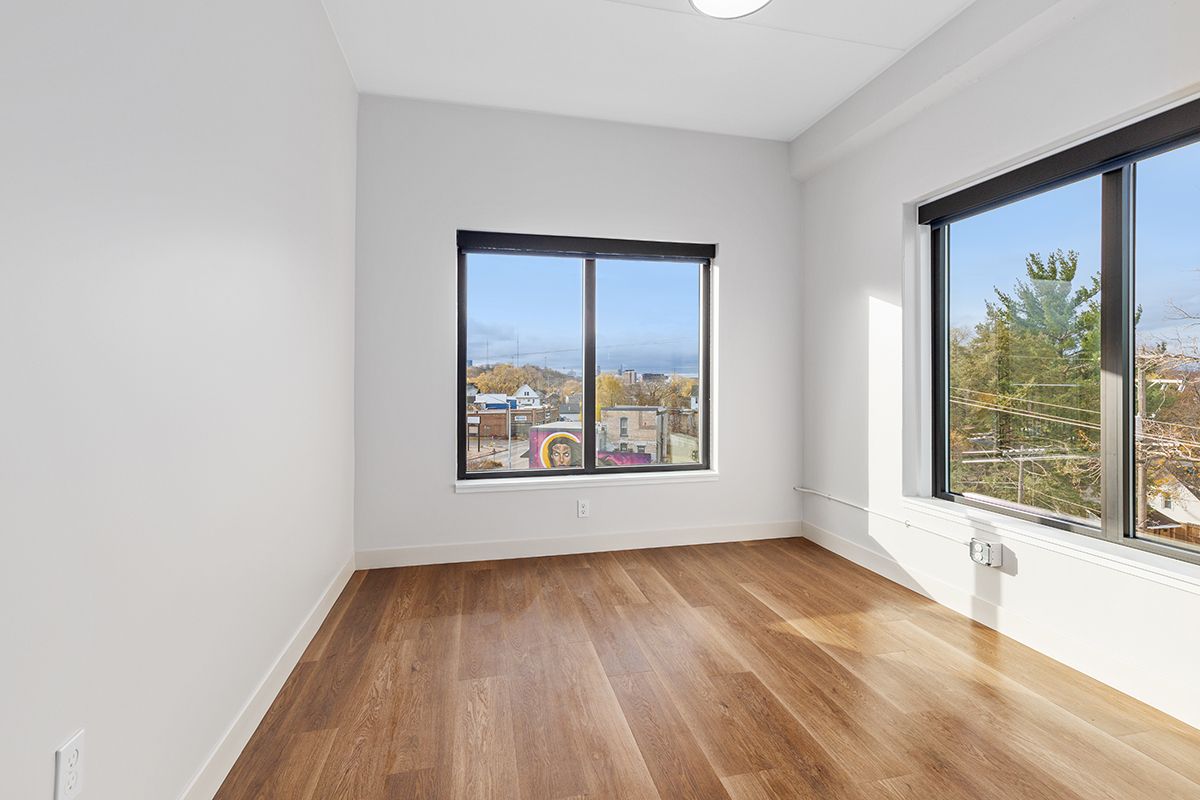 Empty bright room with wood floors, white walls, and two large windows with city and mountain views