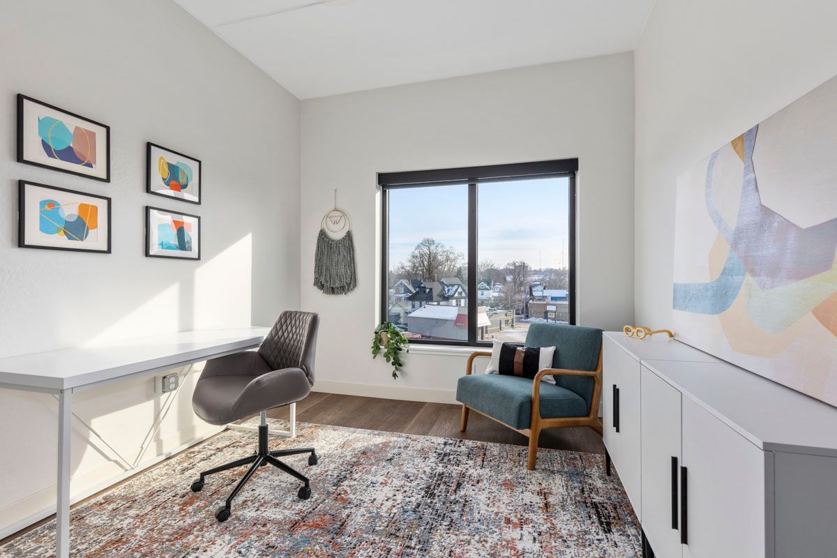 Bright home office with desk, chair, rug, armchair, wall art, and a window overlooking snowy trees.