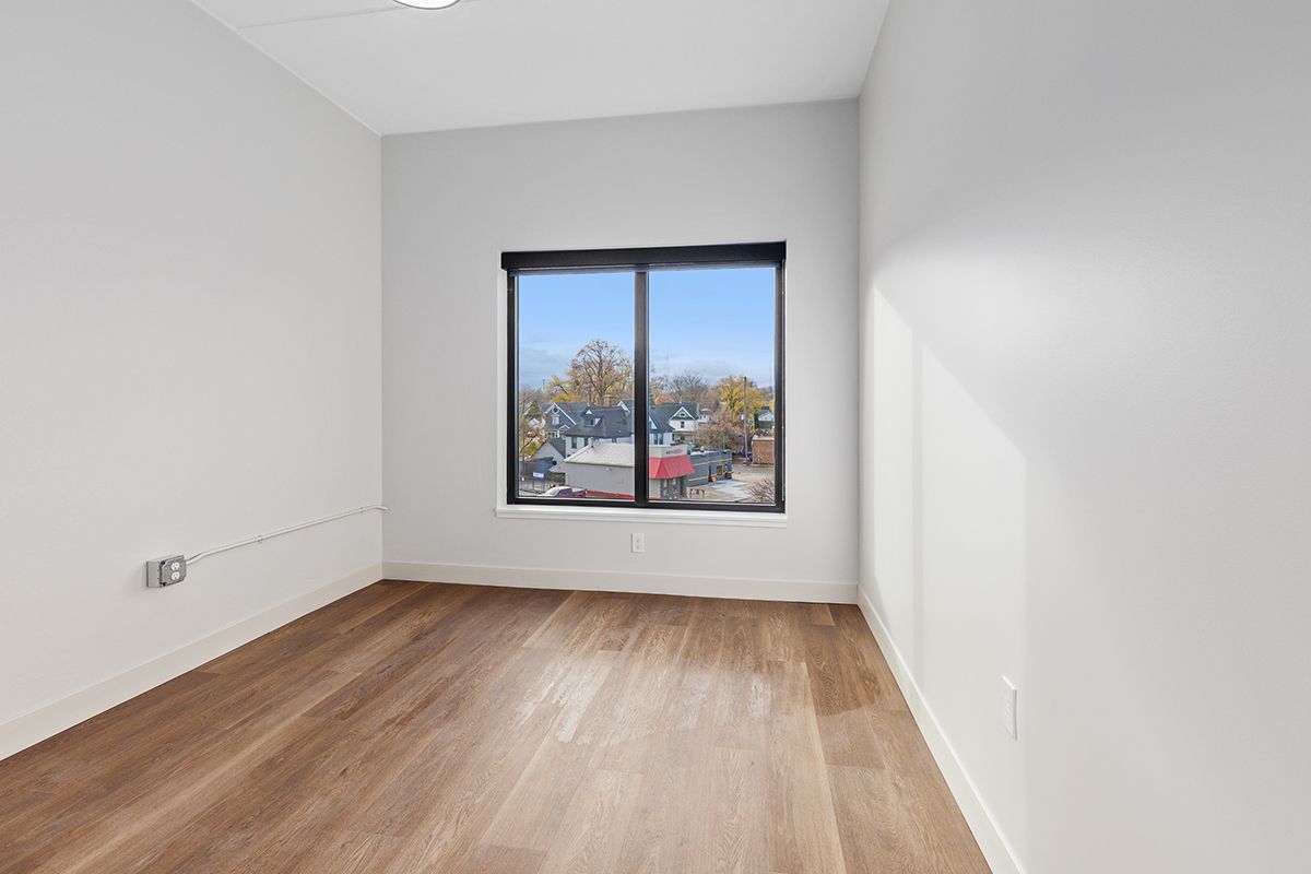 Empty white room with wood floors and a window overlooking trees and buildings