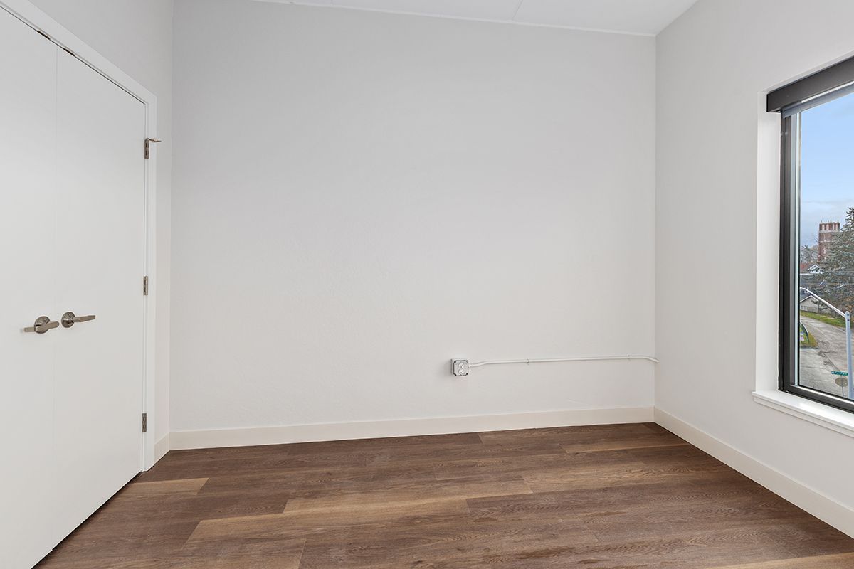 Empty white room with wood floor and a large window on the right.