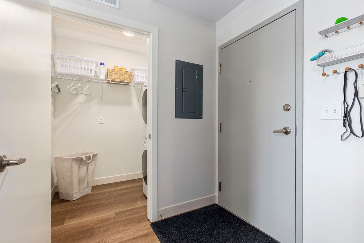 Interior hallway with white door, open closet, wall-mounted panel, and entry mat on wood floor