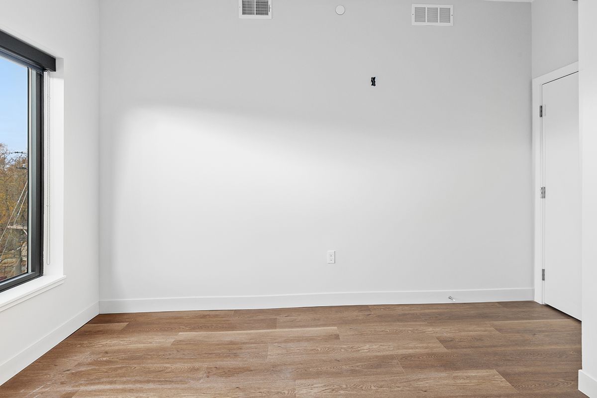 Empty white room with a wood floor and a large window on the left.