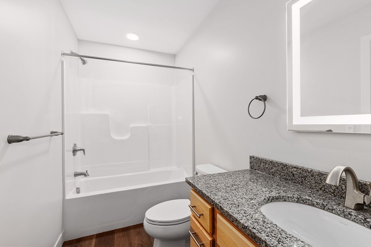 Small bathroom with white tub-shower, toilet, granite vanity, and wall mirror.