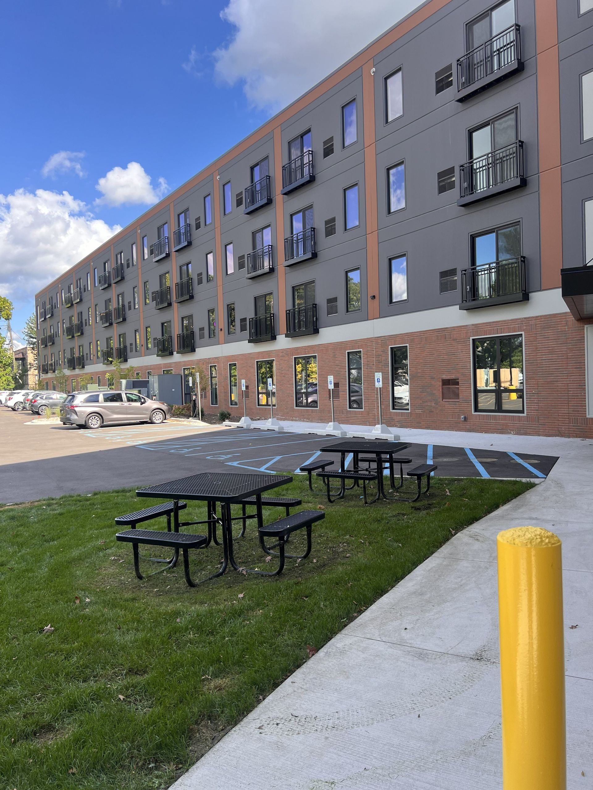 Modern apartment building with balconies, a grassy courtyard, and picnic tables under a blue sky