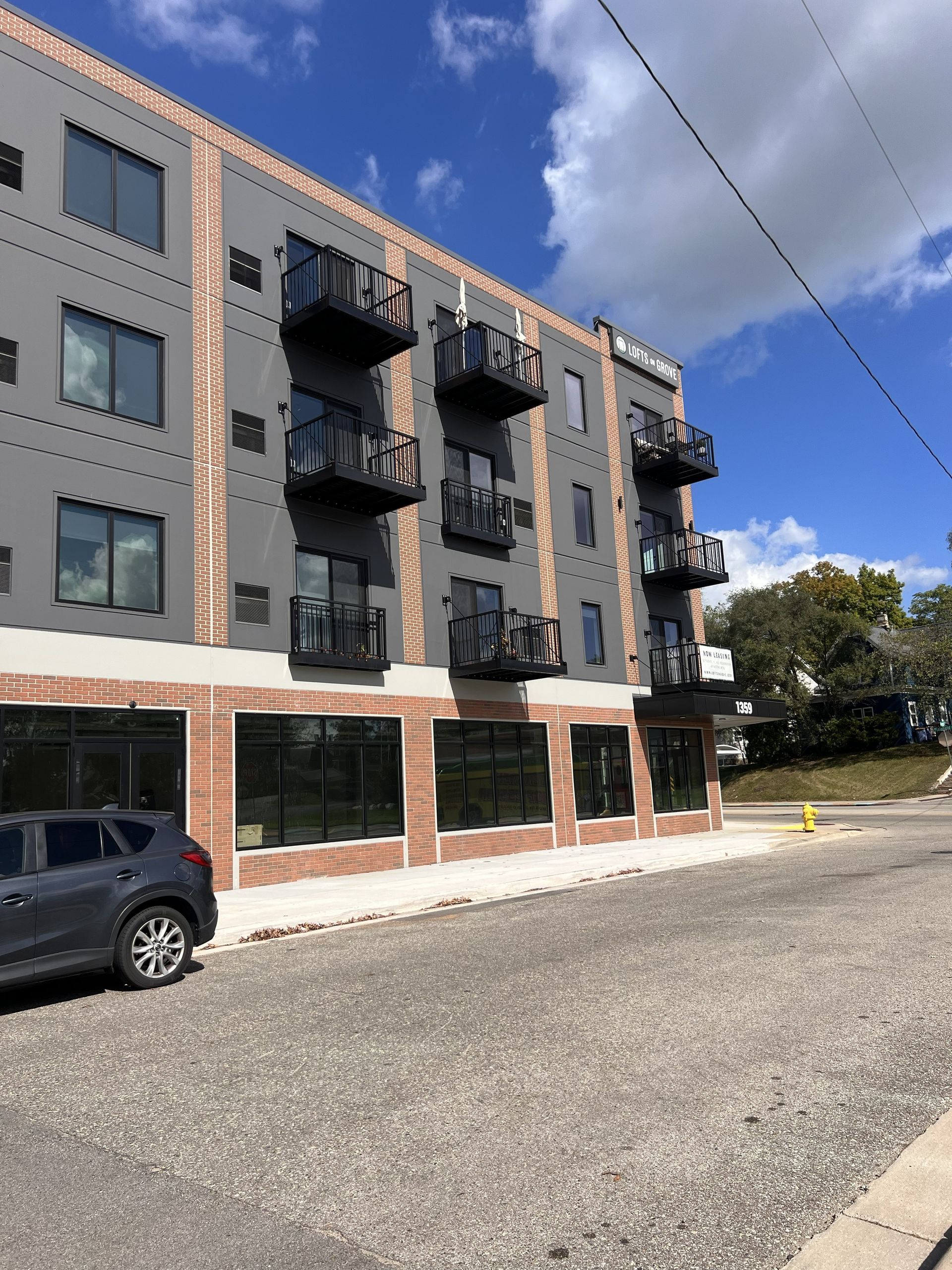 Apartment building with black balconies and parked SUV beside a gravel lot under a blue sky