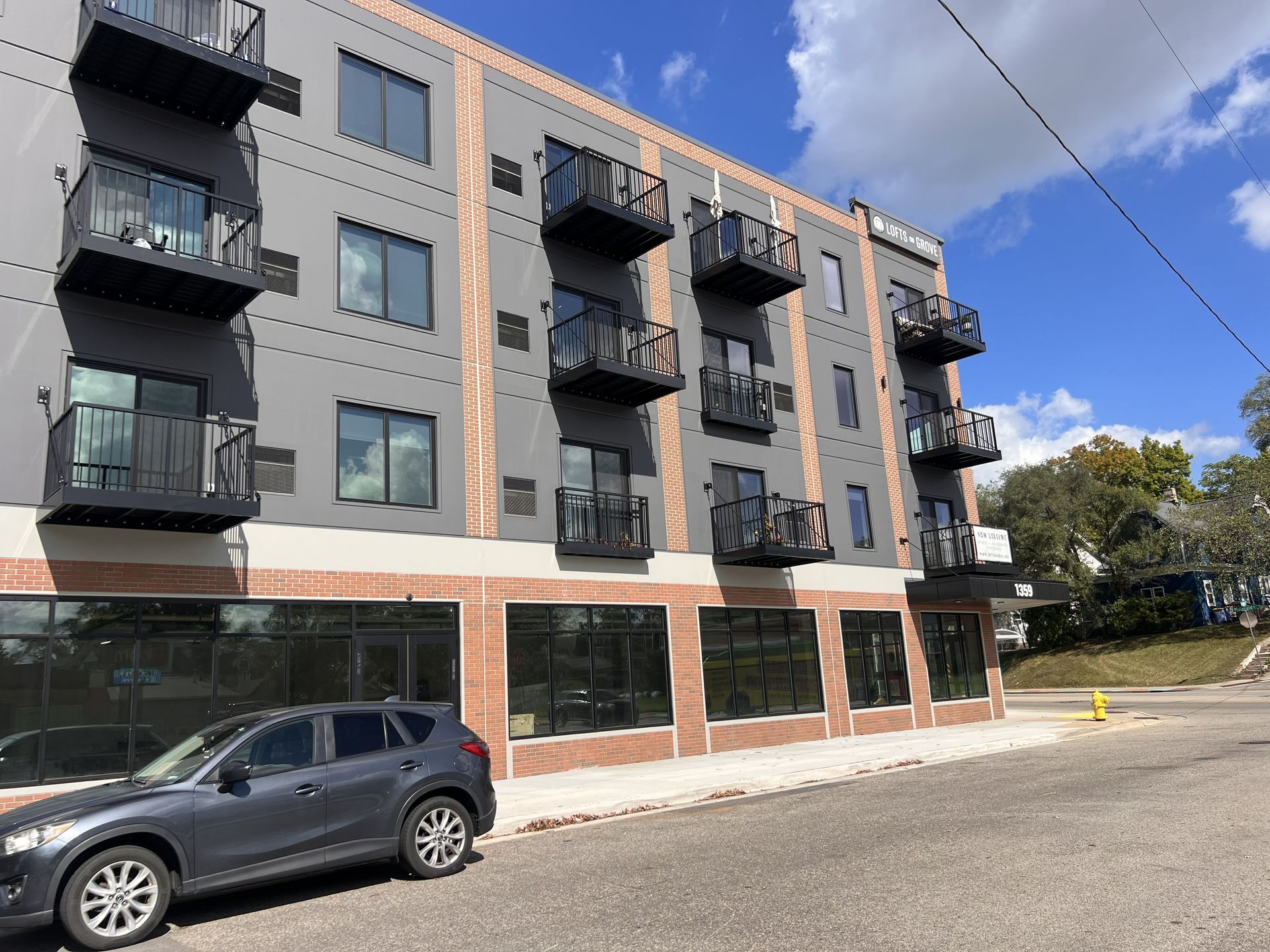 Modern apartment building with dark balconies and a parked car along a quiet street under a blue sky