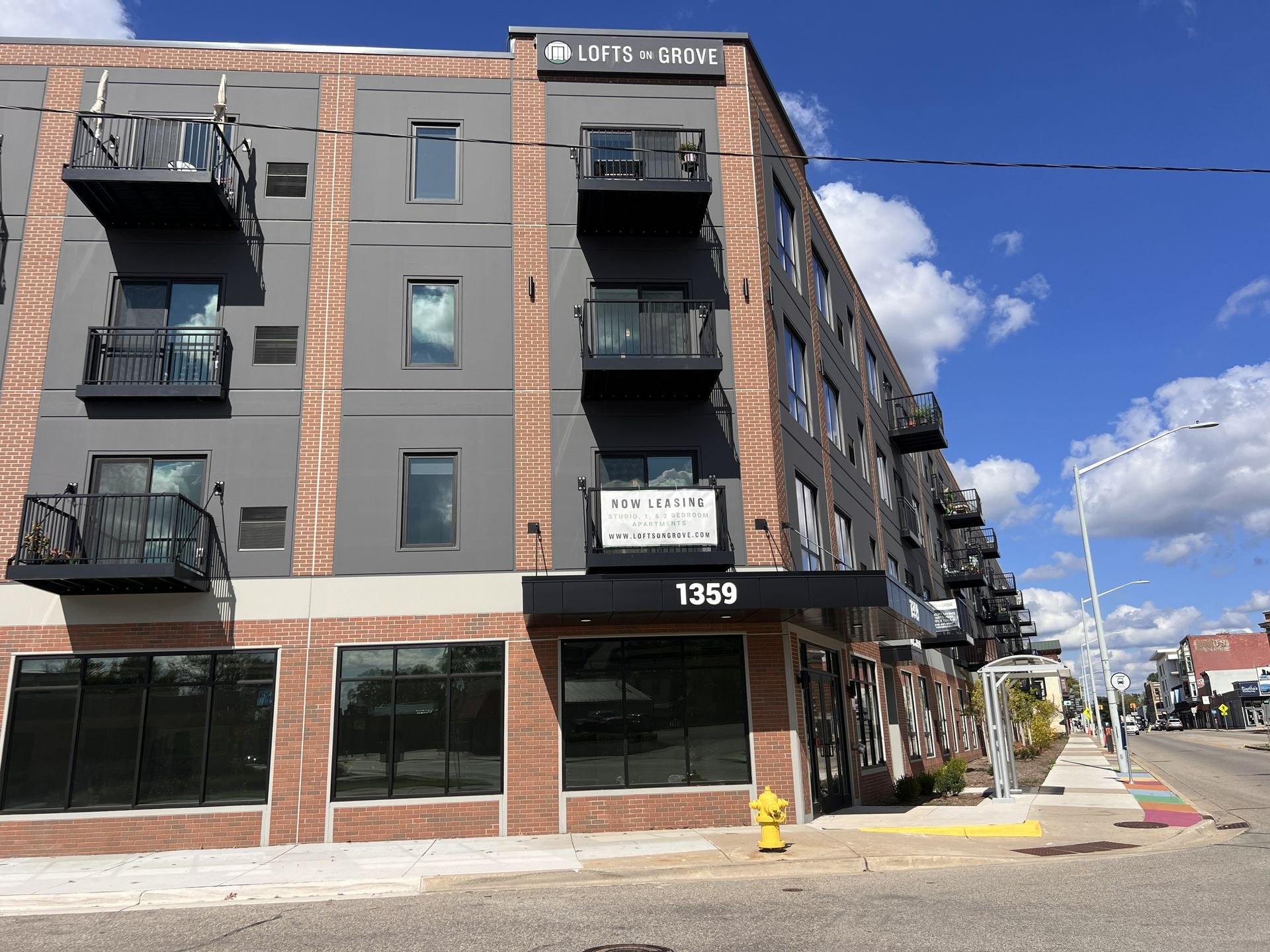 Corner apartment building with black balconies and brick facade under a blue sky