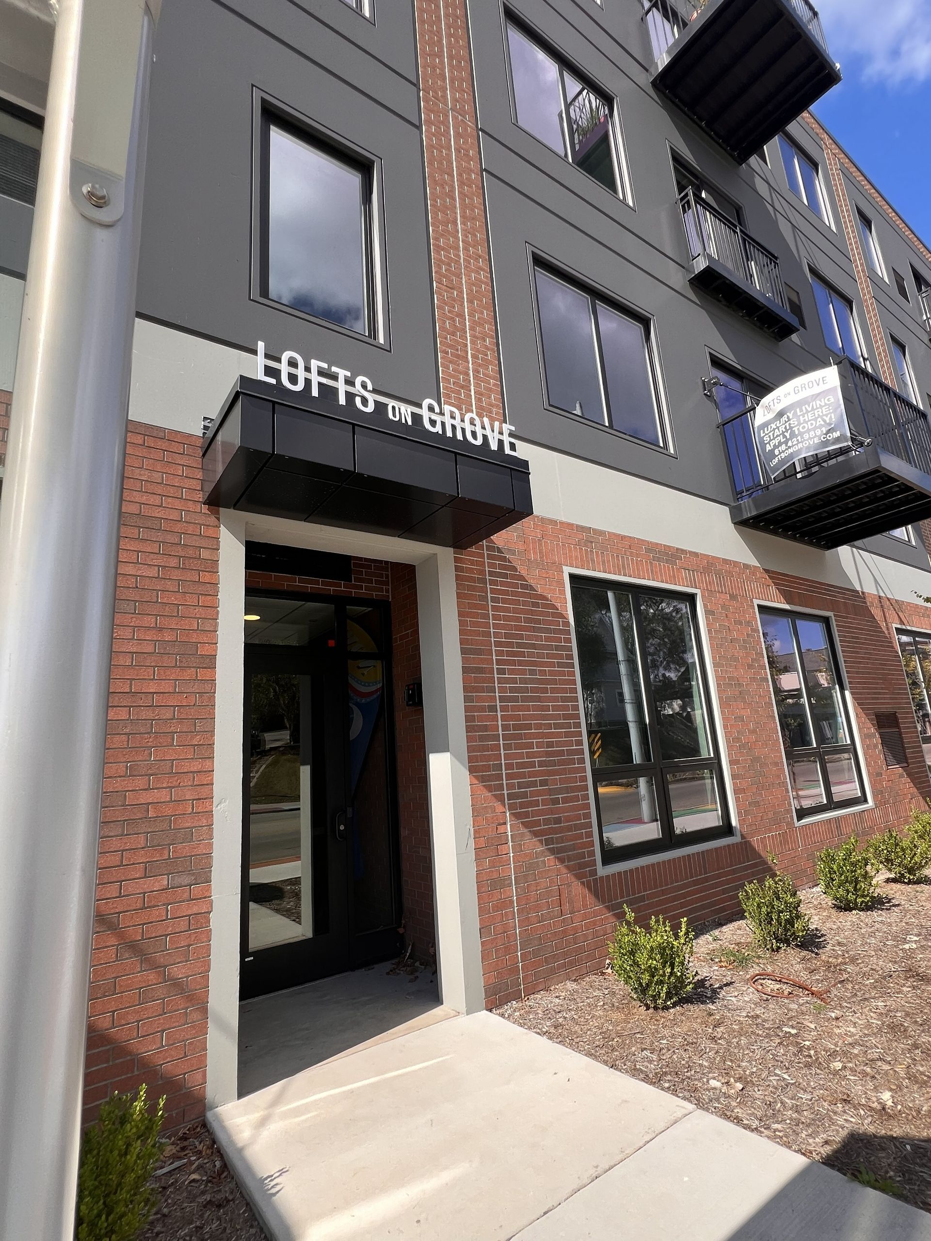 Apartment building entrance with black awning, brick facade, and concrete walkway