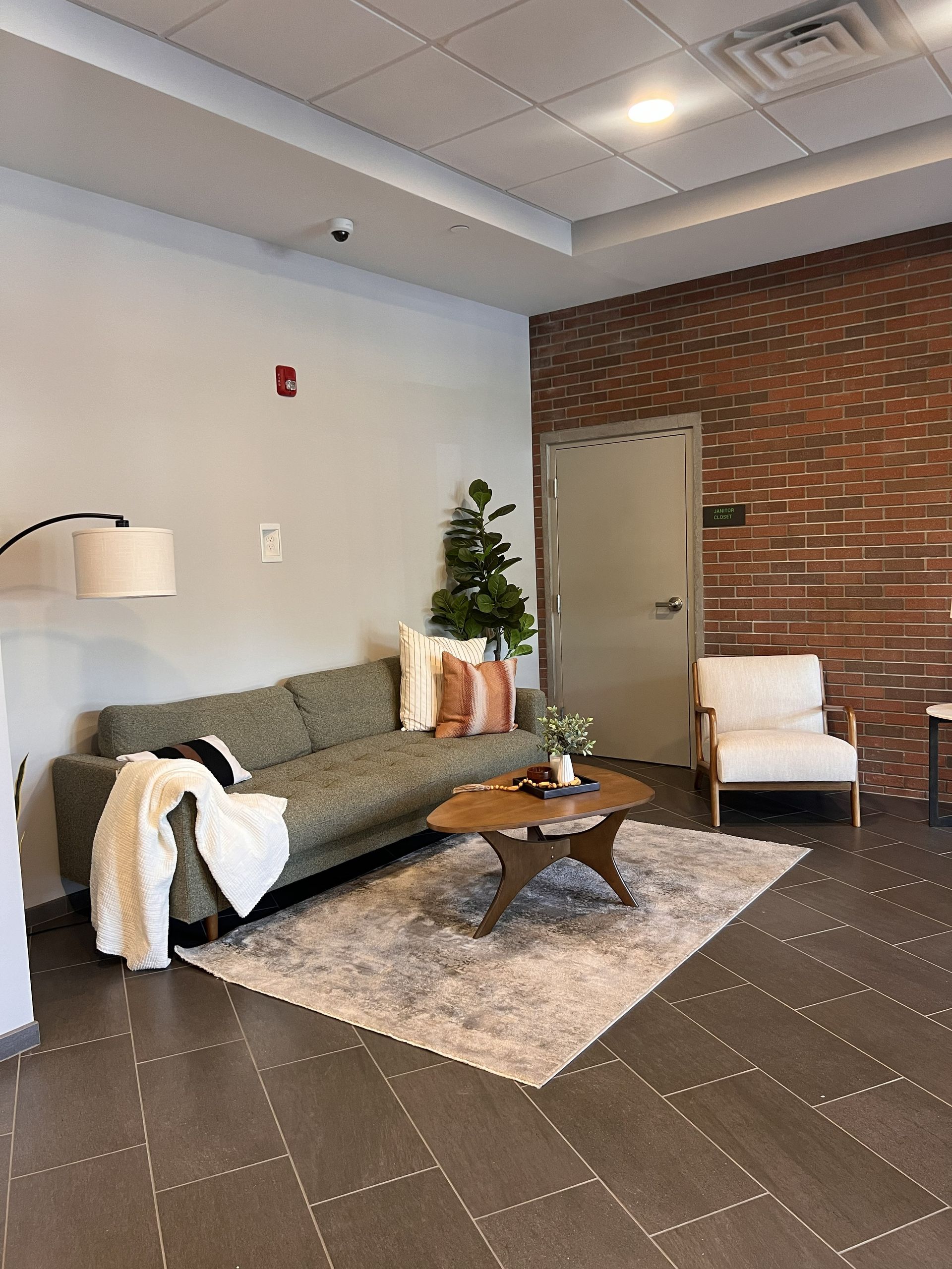Modern lobby with green sofa, armchair, coffee table, rug, floor lamp, and brick accent wall