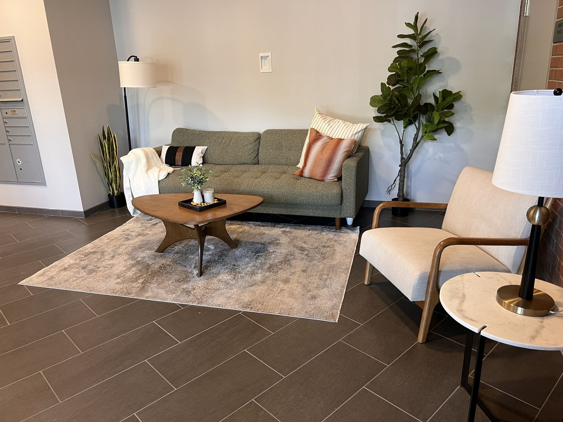 Modern living room with gray sofa, beige chair, round tables, rug, and potted plant