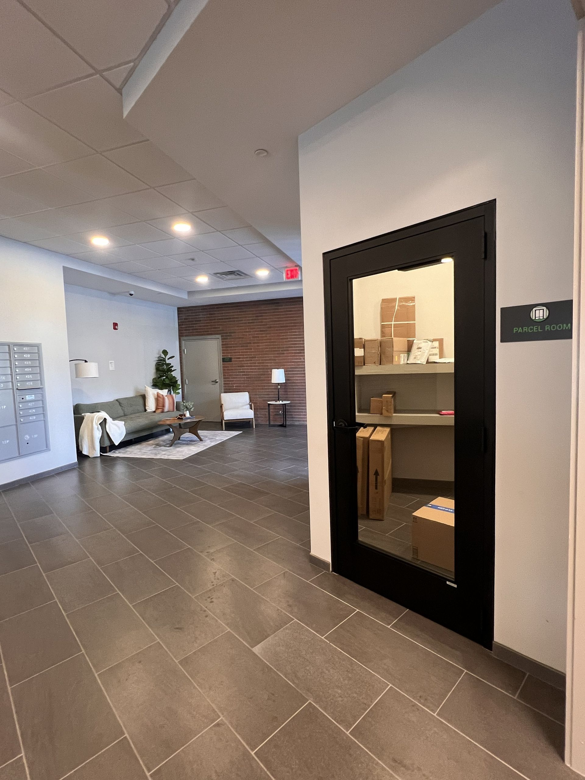 Office hallway with dark tile floor, white walls, a small reception area, and a black-framed doorway.