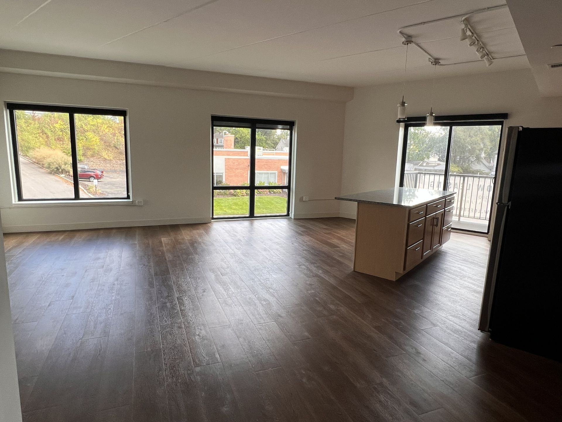 Empty unfurnished living room with wood floors, windows, and a sliding glass door to a balcony
