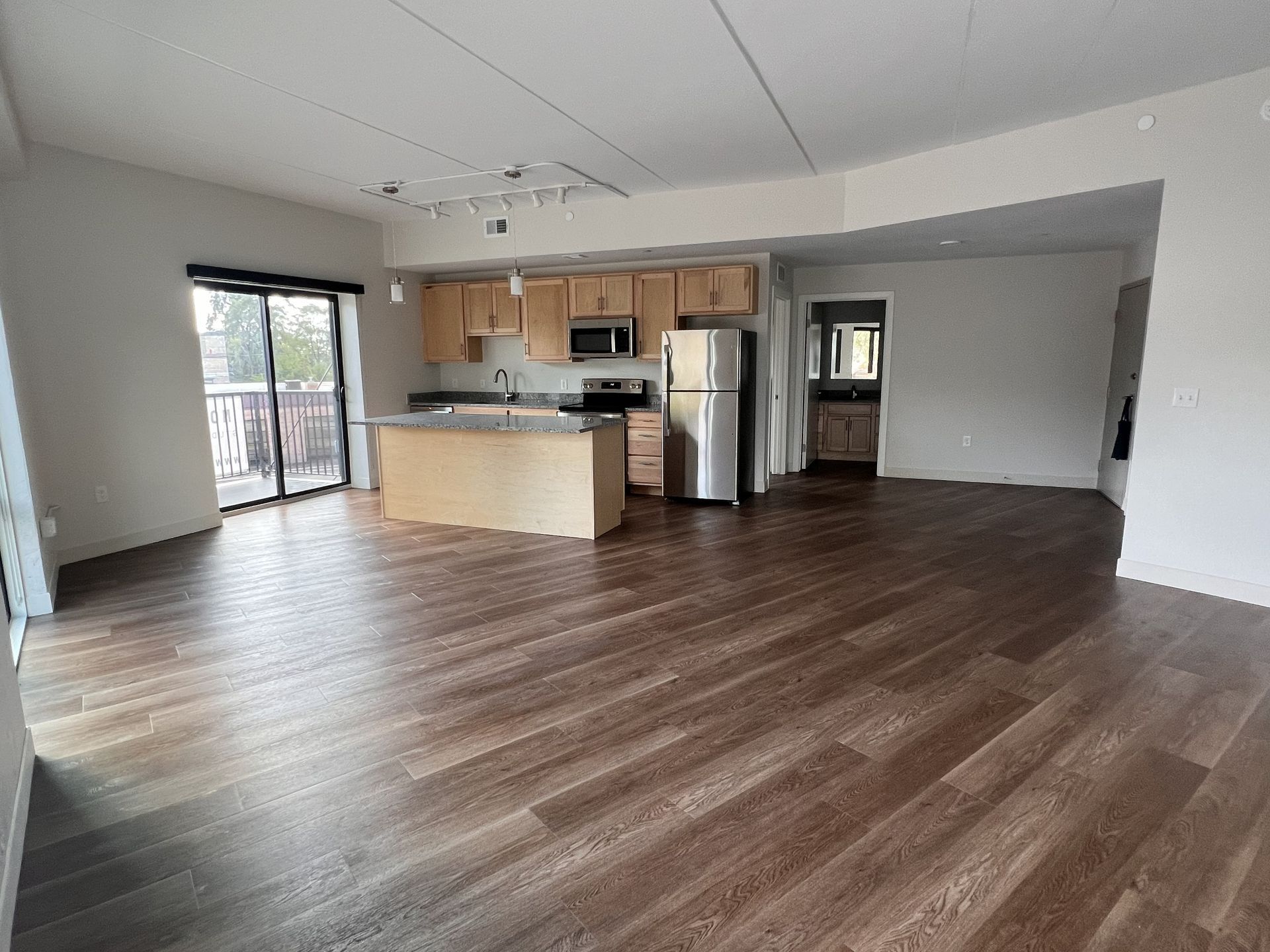 Empty open-plan living room with wood floors and a kitchen island, viewed from the entryway