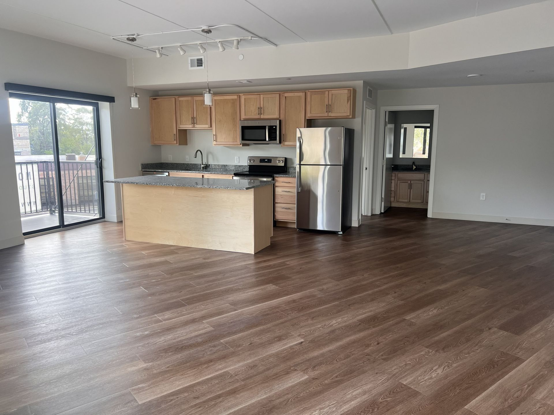 Open-plan kitchen and living room with wood flooring, stainless steel appliances, and sliding glass doors.