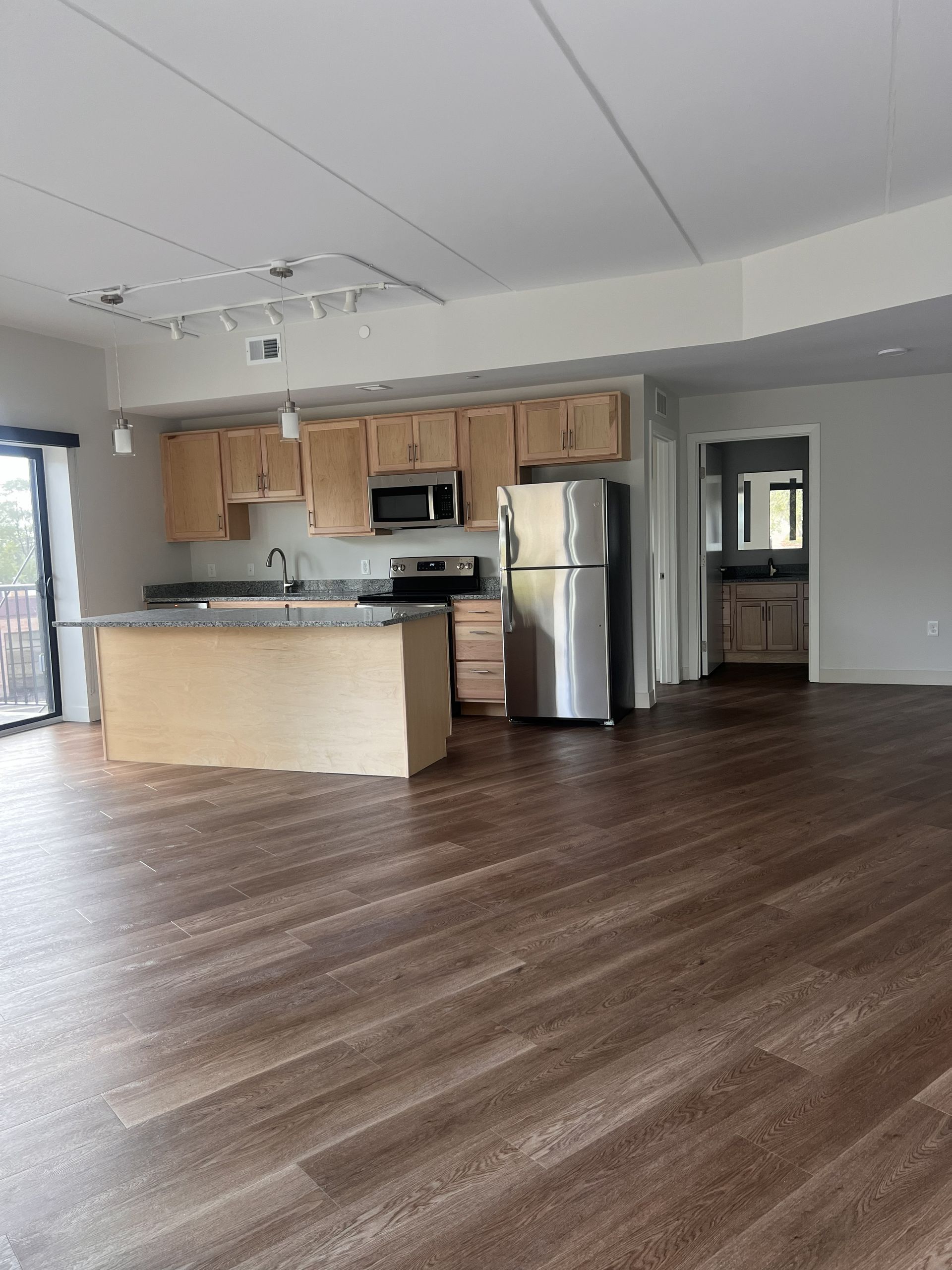 Empty open-concept kitchen and living area with wood floors, light cabinets, and stainless steel appliances